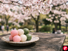 Three-color hanami dango skewer with pink, white and green rice dumplings under cherry blossoms